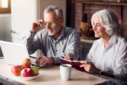 Older couple sitting at table looking at computer. 