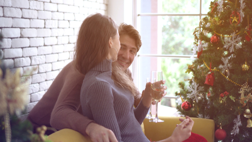 couple sitting by christmas tree with glasses of champagne 