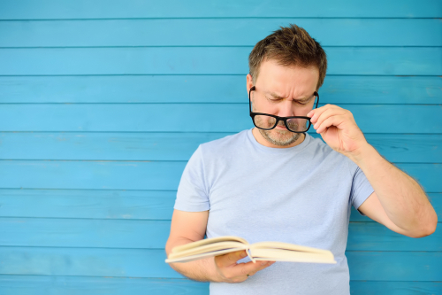 man holding glasses while reading a book 